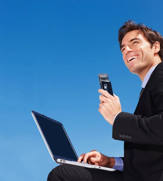 Бизнесмен использует ноутбук, держа в руках мобильный телефон. Успешный молодой бизнесмен с ноутбуком в руках мобильного телефона. — стоковое фото