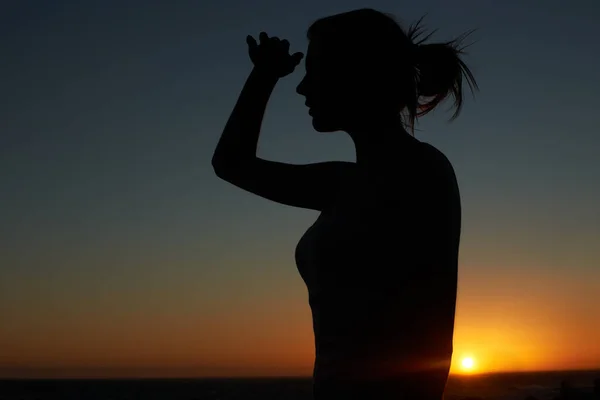 Hasta donde alcanza la vista. Silueta de una mujer joven mirando a la distancia contra un sol poniente. — Foto de Stock