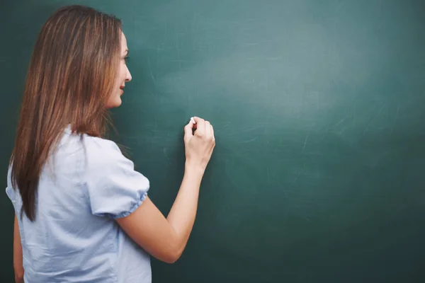 De les voor vandaag is... Een mooie jonge leraar die een lessenplan schrijft op het schoolbord. — Stockfoto