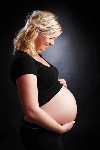 Czuję, jak ciąża świeci. Profil boczny spokojnej kobiety w ciąży trzymającej goły brzuch i patrzącej w dół. — Zdjęcie stockowe