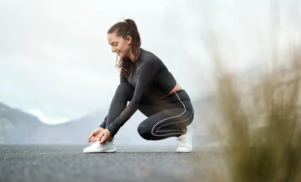 Jag måste se till att de inte är lösa. Full längd skott av en attraktiv ung kvinna knyta sina skosnören innan du tränar utomhus ensam. — Stockfoto