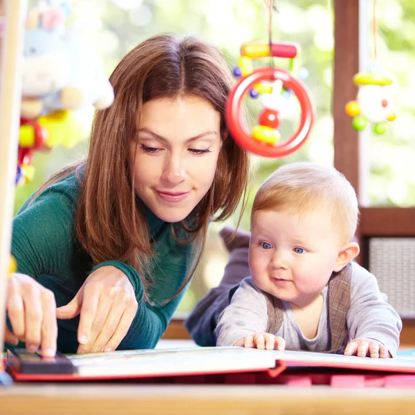 Look at this. Cute young mom lying alongside her infant son on the playroom floor. — Stock Photo, Image