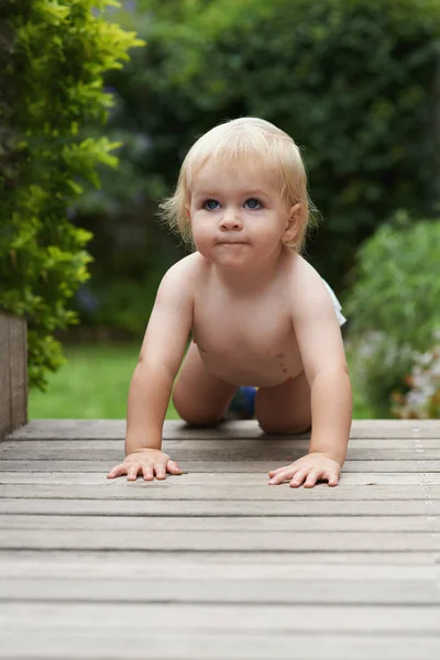 Os bebés primeiro rastejam. Um bebê rastejando ao longo de uma superfície de madeira em um jardim. — Fotografia de Stock