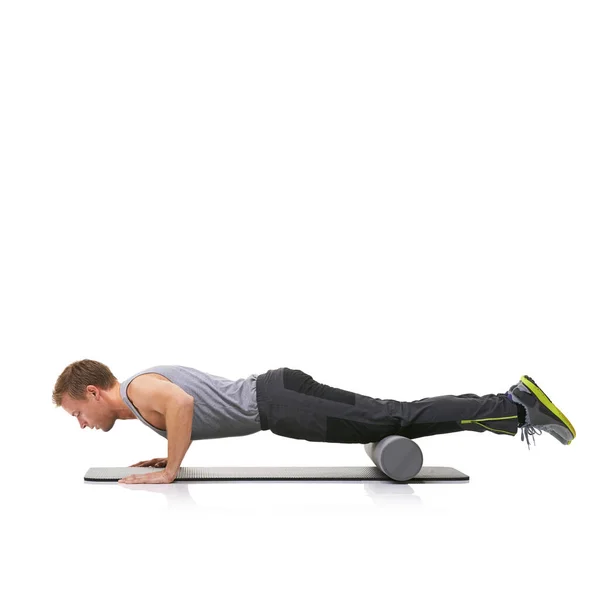 Het verbeteren van zijn kracht en flexibiliteit. Een jonge man doet push-ups op zijn trainingsmat met zijn benen opgevoed door een schuimroller. — Stockfoto