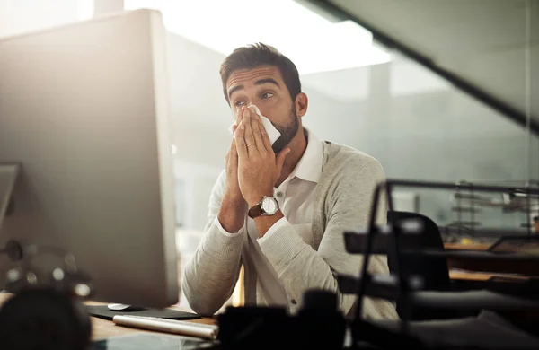 Kan dit de griep zijn? Schot van een knappe jonge zakenman die zijn neus snuit terwijl hij overwerkt in een kantoor.. — Stockfoto