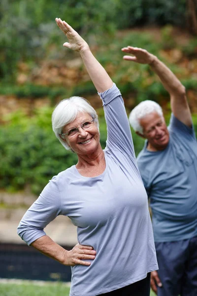 Dehnung in Richtung Gesundheit und Glück. Aufnahme eines älteren Paares beim gemeinsamen Yoga im Freien. — Stockfoto