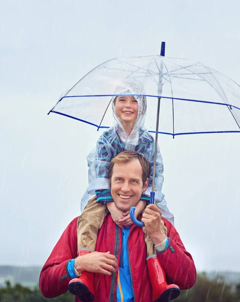 Het weer zal ons niet in de weg staan. Gehakt portret van een vader die zijn zoon buiten op zijn schouders droeg in de regen. — Stockfoto