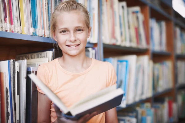 Op een dag word ik schrijver. Portret van een schattig jong meisje dat een boek leest in de bibliotheek. — Stockfoto