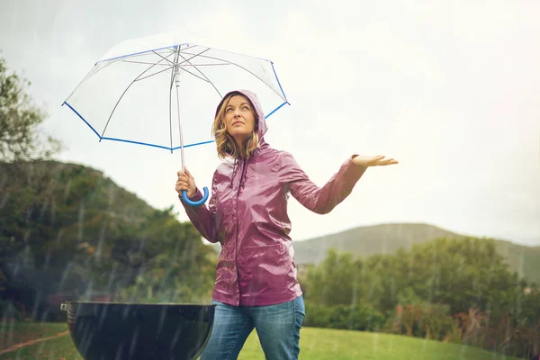 Todo se ve mejor ahora. Foto de una mujer haciendo una barbacoa al aire libre bajo la lluvia mientras sostiene un paraguas y mira hacia el cielo. — Foto de Stock