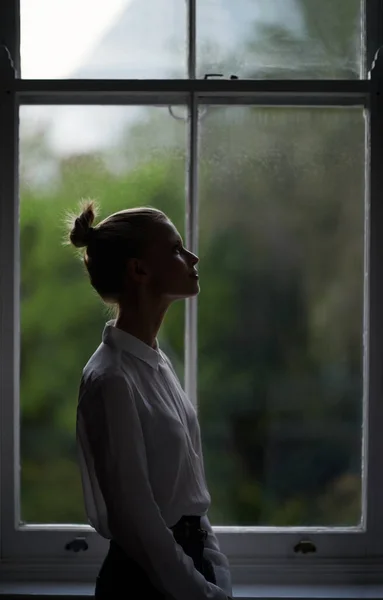Reflexión junto a la ventana. Una hermosa joven de pie junto a una ventana. — Foto de Stock