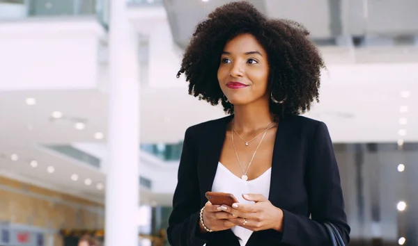 Il suo un accessorio indispensabile per un imprenditore moderno. Girato di una giovane donna d'affari che utilizza uno smartphone mentre cammina attraverso un ufficio moderno. — Foto Stock