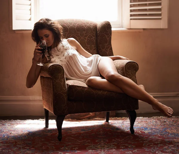 Gönnen Sie sich ein Glas Genuss. Aufnahme einer sexy jungen Frau, die es sich auf einem Sessel bequem macht und ein Glas Wein genießt. — Stockfoto