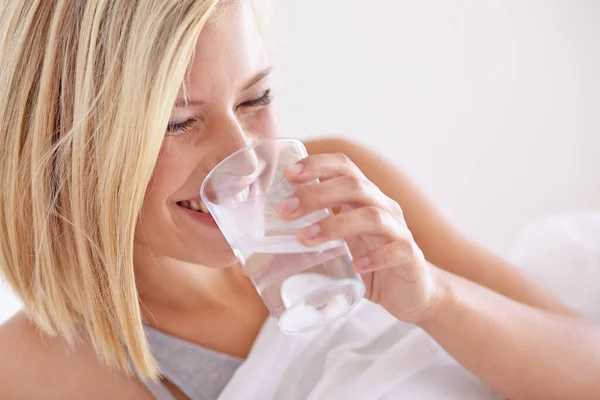 She always drinks a glass of water before bed. A young woman drinking a glass of water before bed.