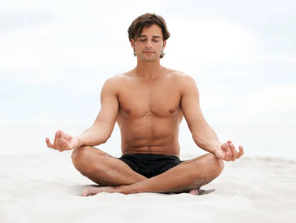 Seid still und hört zu, was die Natur zu sagen hat. Junger schöner Mann sitzt am Strand und meditiert. — Stockfoto