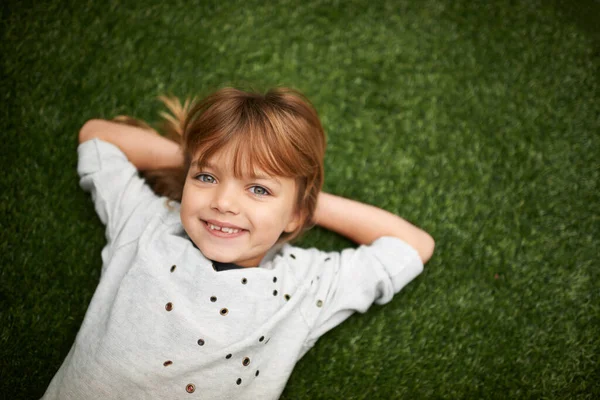 Ein Charmeur. Kleines Mädchen liegt im Gras, die Hände hinter dem Kopf. — Stockfoto