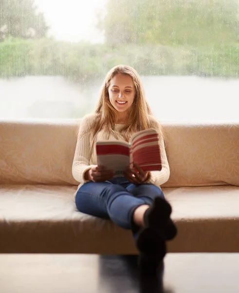 Наслаждаюсь хорошей книгой. Фотография привлекательной молодой женщины, читающей книгу, сидя дома на диване. — стоковое фото