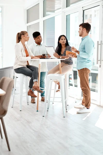 Discussões informais. Tiro de comprimento cheio de um grupo de colegas de negócios jovens reunidos em volta de uma mesa no seu escritório. — Fotografia de Stock