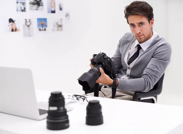 Fotógrafo jovem e criativo. Retrato de um fotógrafo sentado em uma mesa em seu escritório segurando uma câmera. — Fotografia de Stock