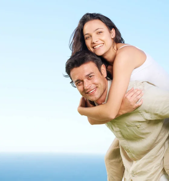 Beru ji na vyhlídku. Mladý muž piggybacking jeho přítelkyně s výhledem na oceán v pozadí. — Stock fotografie