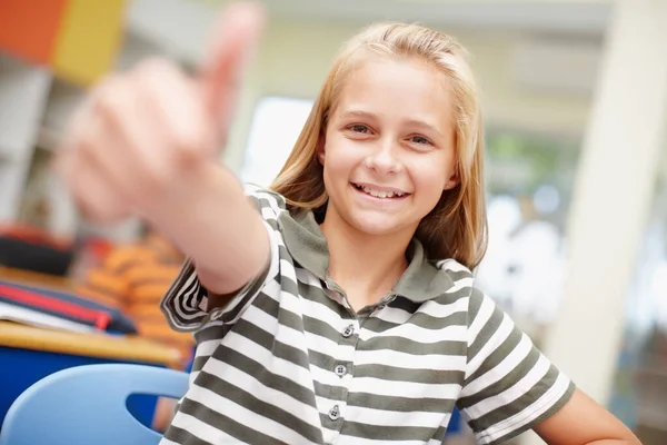 Moje škola je úžasná. Sladké základní škola dívka dává palce nahoru - soustředit se na pozadí. — Stock fotografie