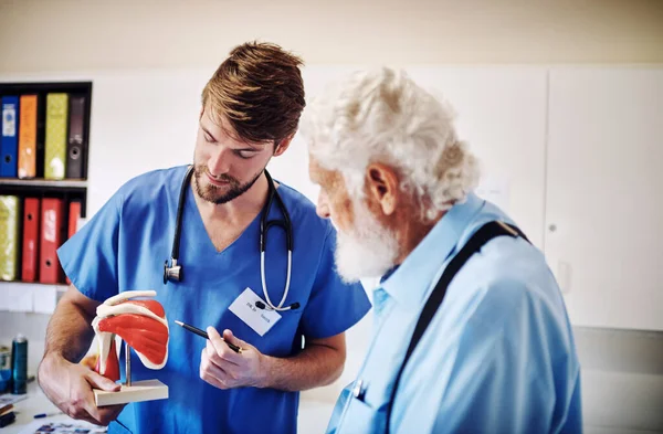 El tratamiento que estás empezando va a combatir esta área. Inyección de un médico joven usando un modelo para explicar un diagnóstico a su paciente mayor. — Foto de Stock