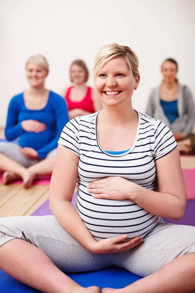 Mijn focus ligt op een kalme geboorte. Een groep zwangere vrouwen zit gekruiste benen in een yogales en glimlacht vrolijk. — Stockfoto