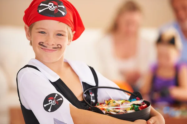 Una cesta llena de golosinas. Un niño pequeño vestido con un disfraz de pirata y sosteniendo una canasta de dulces con la familia sentada en el fondo. — Foto de Stock