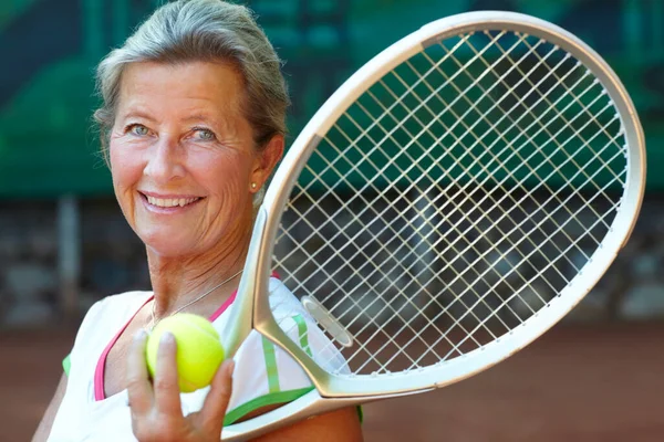 Tennis is her game. Senior woman smiling while holding a tennis racquet and ball.