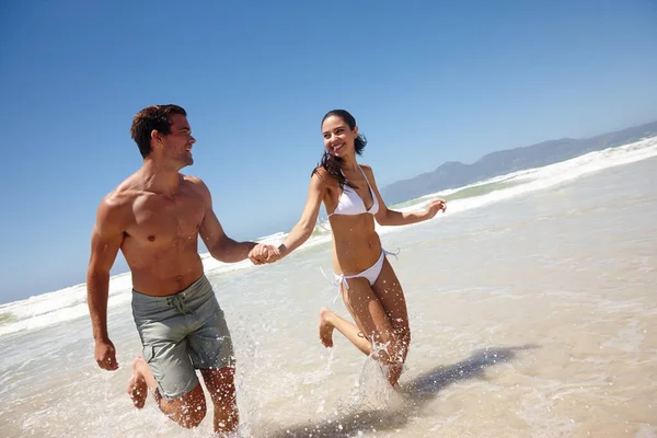 Denk aan ons eerste afspraakje. Shot van een gelukkig jong koppel dat door het water loopt. — Stockfoto