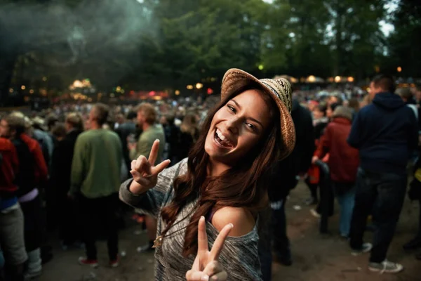 Chodzi o wibracje. Ładna młoda kobieta pokazująca znak pokoju na festiwalu muzyki na świeżym powietrzu. — Zdjęcie stockowe
