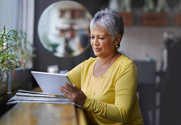 Technologie hilft ihr, mit Freunden in Kontakt zu bleiben. Aufnahme einer reifen Frau mit einem digitalen Tablet in einem Café. — Stockfoto