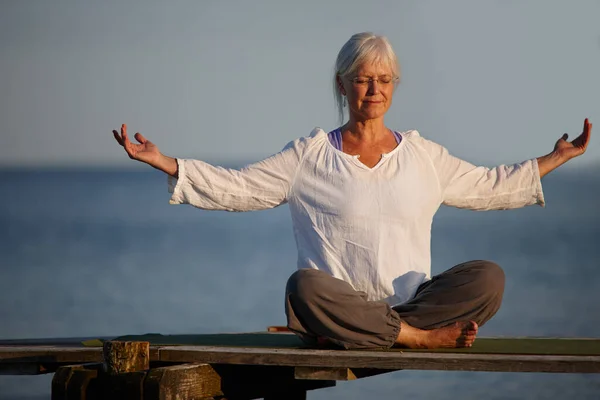 Bli lugn som havet. Full längd skott av en attraktiv mogen kvinna som gör yoga på en pir ute på havet. — Stockfoto