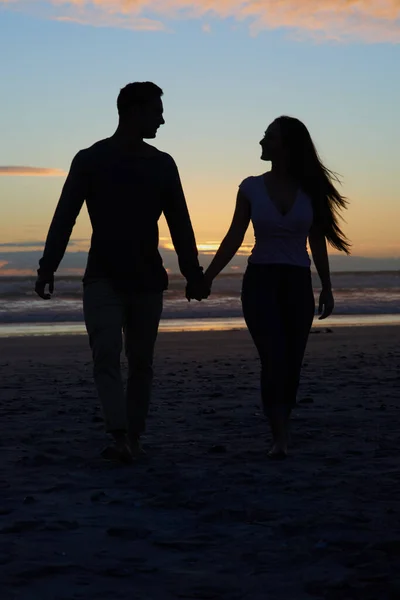 Det bästa med solnedgångar är att se dem med dig. Silhuett skott av ett ungt par promenader på stranden. — Stockfoto