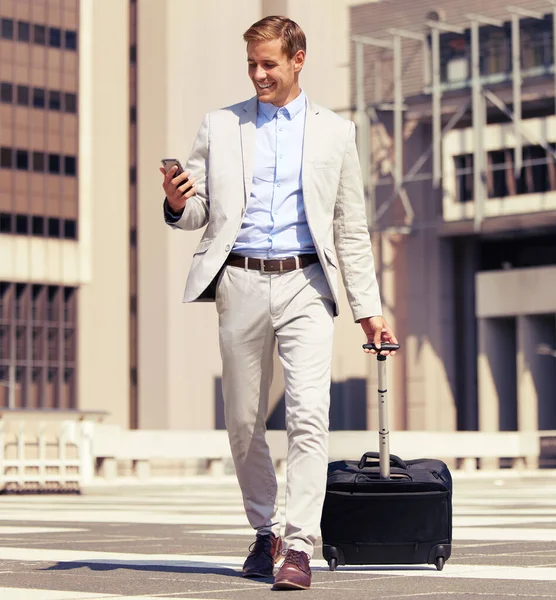Questa applicazione è conveniente per un uomo d'affari in movimento. Girato di un giovane uomo d'affari che usa un cellulare mentre cammina con una valigia in città. — Foto Stock
