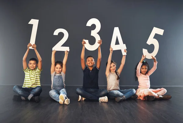 Primera regla del aprendizaje Diviértete. Retrato de estudio de un grupo diverso de niños sosteniendo números sobre un fondo gris. —  Fotos de Stock