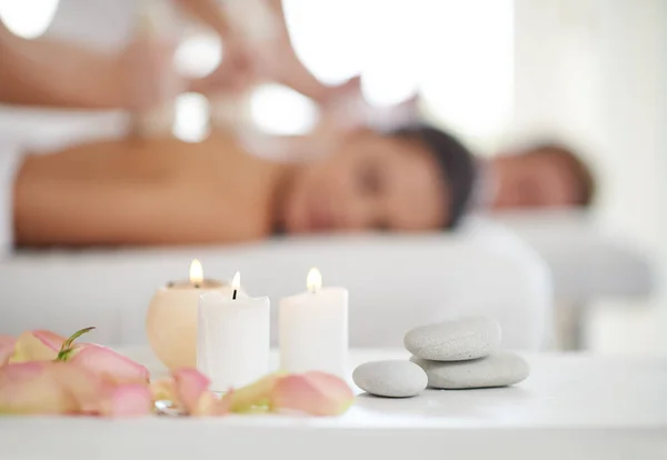 Relaxamento feliz. Um casal recebendo massagens em um spa com velas em primeiro plano. — Fotografia de Stock