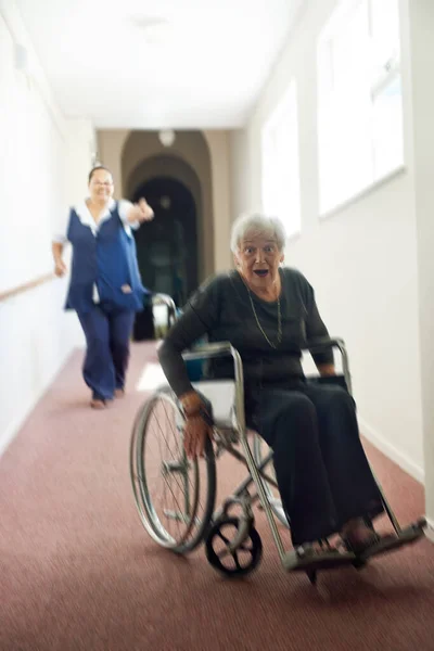 Im Zerplatzen aus diesem Gelenk. Aufnahme einer verschmitzten Seniorin, die mit ihrem Rollstuhl vor ihrer Krankenschwester in einem Altersheim davonläuft. — Stockfoto