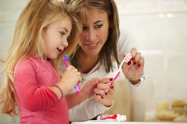 This will keep your teeth healthy. Cute little girl getting ready to brush her teeth with her mom. — Stock Photo, Image