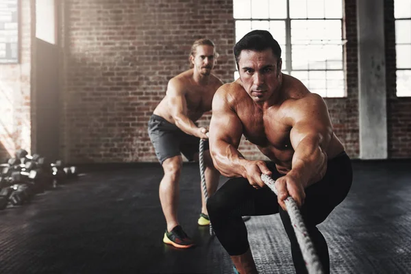 This is what fit and fierce looks like. Shot of two muscular young men pulling on a rope in a gym. — Stock Photo, Image