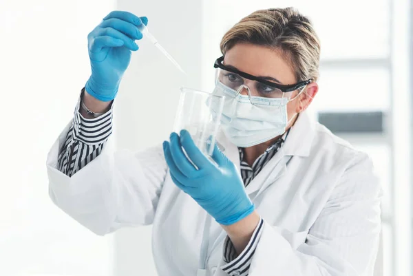 Μόνο λίγες σταγόνες αρκούν. Καλλιεργημένη λήψη μιας ελκυστικής νεαρής γυναίκας επιστήμονα που ρίχνει υγρό δείγμα σε ποτήρι ζέσεως ενώ εργάζεται σε εργαστήριο. — Φωτογραφία Αρχείου