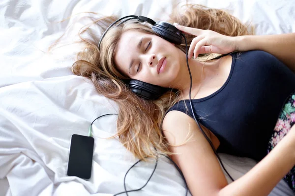 これは私のお気に入りの曲です。ベッドでリラックスしながら音楽を聴く美しい若い女性のショット. — ストック写真