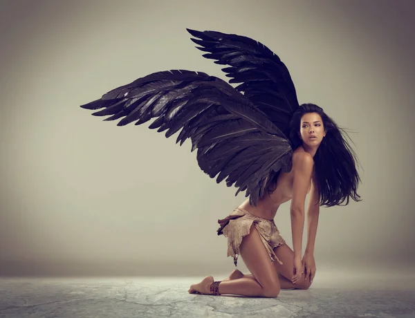 Темний ангел краси. Постріл жінки з крилами на колінах на сірому фоні . — стокове фото