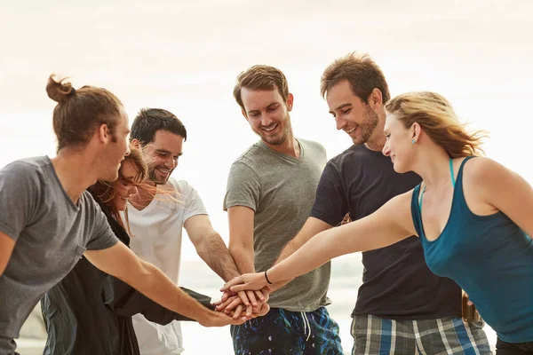 Reunidos pelo seu amor pelo mar. Tiro de um grupo de jovens amigos felizes colocando as mãos em uma pilha na praia. — Fotografia de Stock