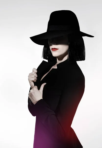 Verborgen in de schaduw. Studio shot van een mysterieuze vrouw met een hoed tegen een grijze achtergrond. — Stockfoto