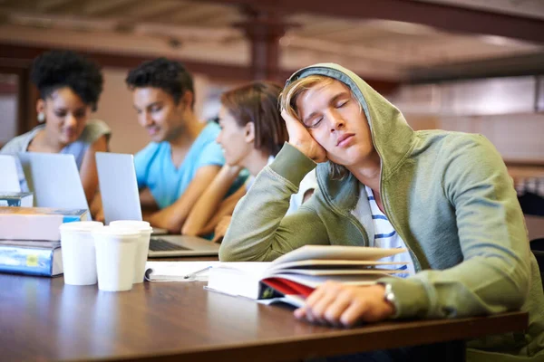 Estudar aborrece-o. Um jovem estudante olhando entediado enquanto em seus colegas de classe estudar int o fundo. — Fotografia de Stock