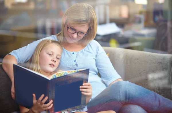 Το αγαπημένο μου βιβλίο. Ένα χαριτωμένο νεαρό κορίτσι κάθεται δίπλα στη μητέρα της, ενώ διαβάζουν ένα βιβλίο. — Φωτογραφία Αρχείου