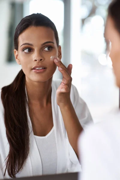 Dobra pielęgnacja skóry jest podstawą jej rutyny piękności. Piękna młoda kobieta nakłada makijaż na jej nieskazitelną skórę w lustrze. — Zdjęcie stockowe