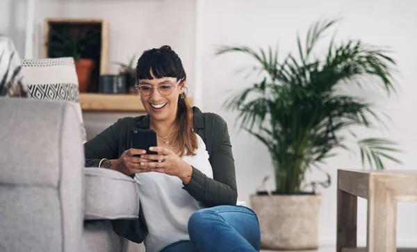 Teknoloji bizi birbirimize bağlıyor. Oturma odasında yalnız başına oturan ve cep telefonunu kullanan çekici genç bir kadının görüntüsü.. — Stok fotoğraf
