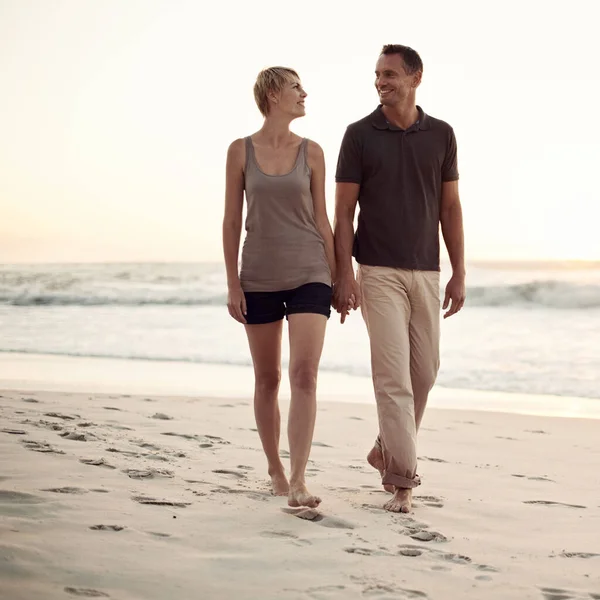 Ils adorent les longues promenades sur la plage. Tourné d'un couple d'âge mûr faisant une promenade sur la plage. — Photo