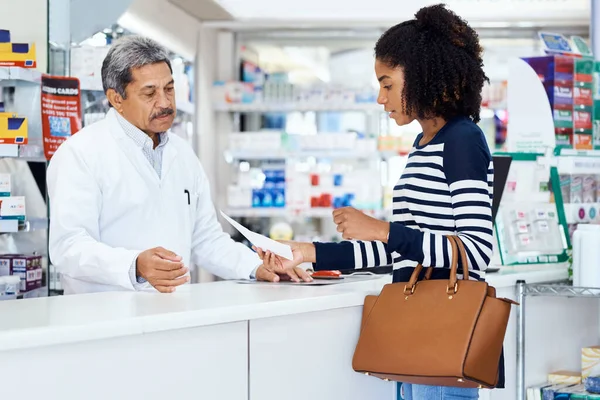 J'ai besoin des médicaments suivants s'il vous plaît. Prise de vue d'un pharmacien assistant une jeune femme dans un chimiste. — Photo